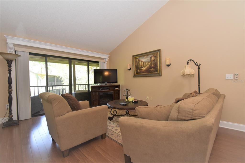 A living room features beige walls, wood-look flooring, a sofa, an armchair, and a television — 1637 BROOKHOUSE COURT UNIT BR243, SARASOTA, FL