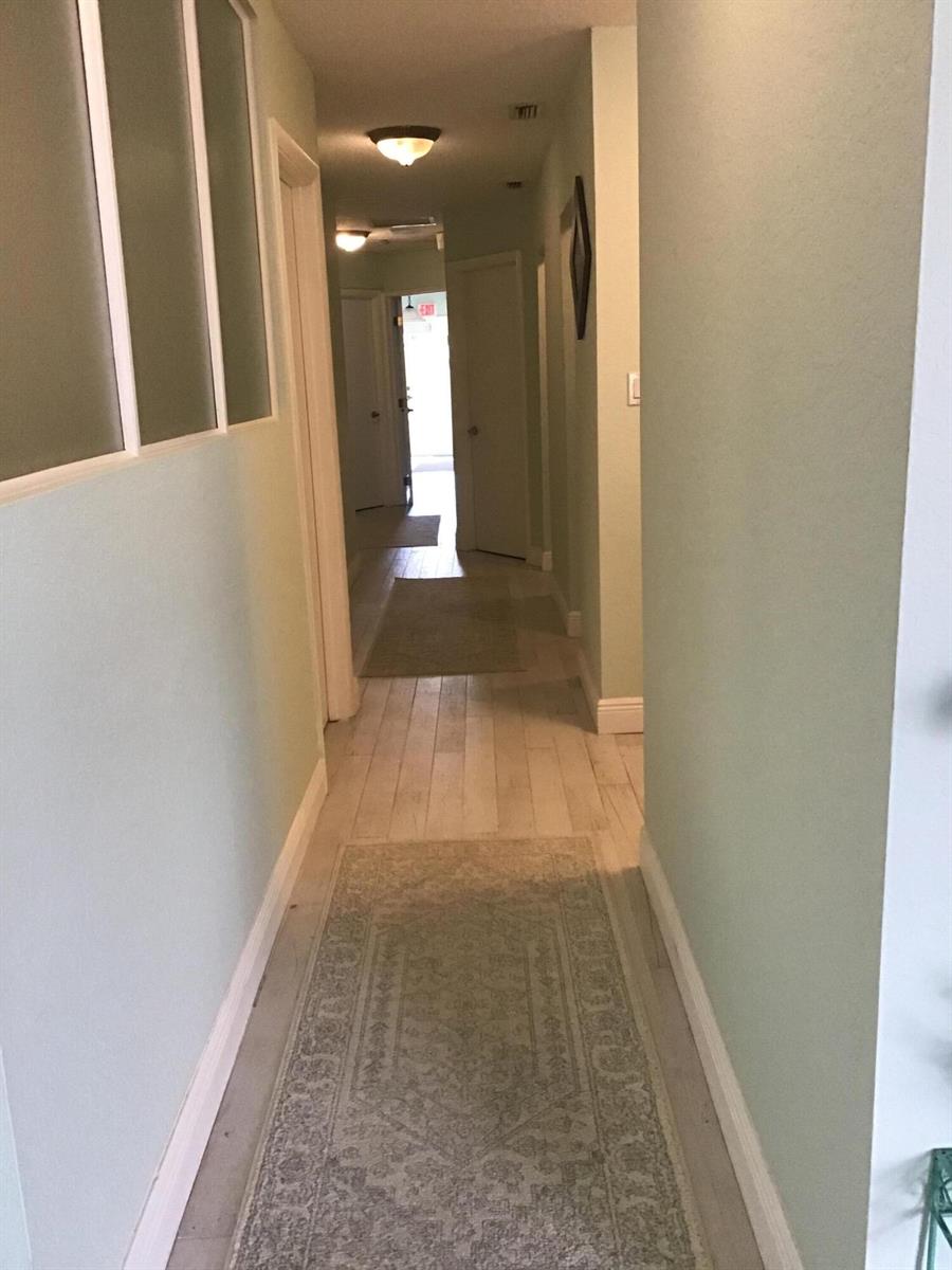 A long hallway with light-colored wood flooring, pale green walls, and two area rugs — 812 SE 8th Avenue, Deerfield Beach FL 33441, DEERFIELD BEACH, FL