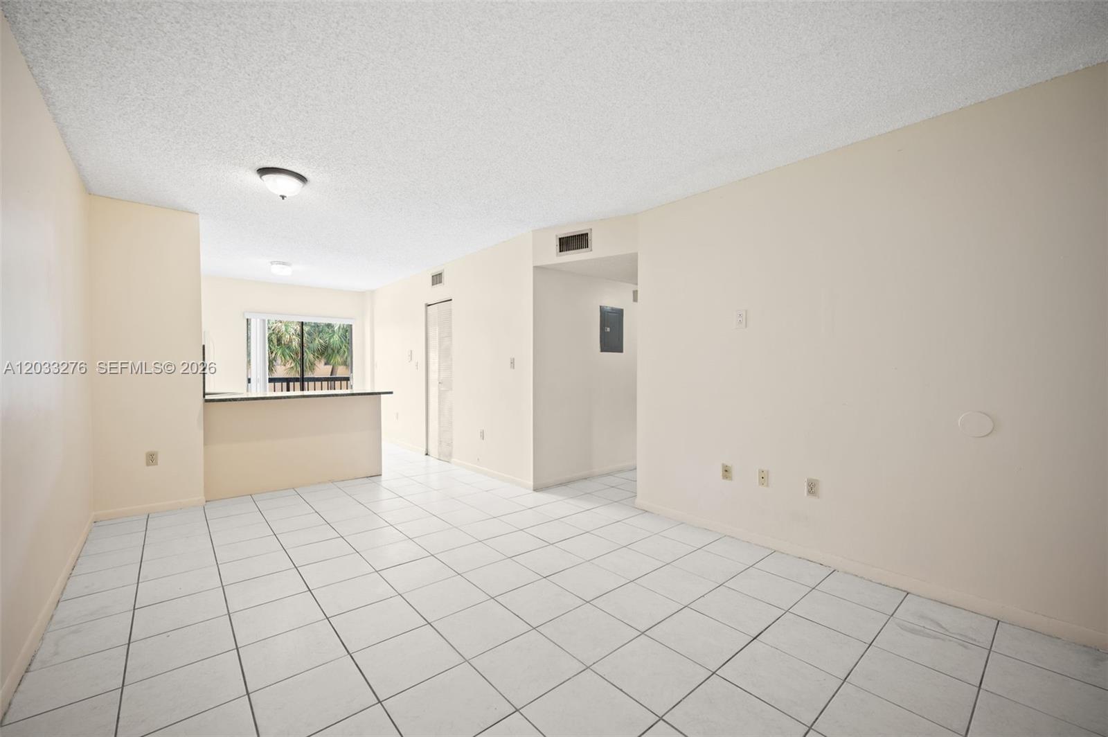 An empty room with white tiled floors, beige walls, and a kitchen pass-through window — 5490 W 21st Ct # 310, Hialeah FL 33016, HIALEAH, FL