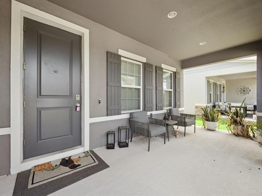 A covered front porch features a gray door, two chairs, and potted plants — 137 LAVENNA AVENUE, ST CLOUD, FL