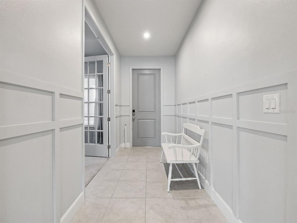 A hallway with light tile flooring, white wainscoting, a white bench, and a gray door — 137 LAVENNA AVENUE, ST CLOUD, FL