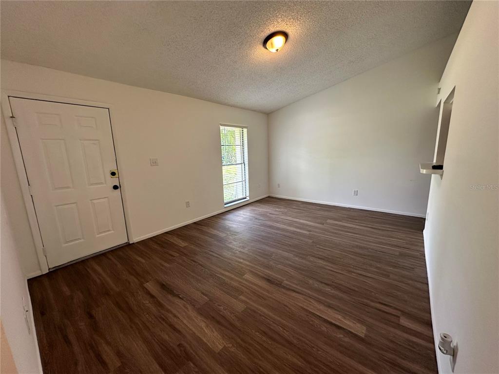 An empty room features wood-look flooring, white walls, a vaulted ceiling, and a single window — 1928 BONNEVILLE DRIVE, ORLANDO, FL