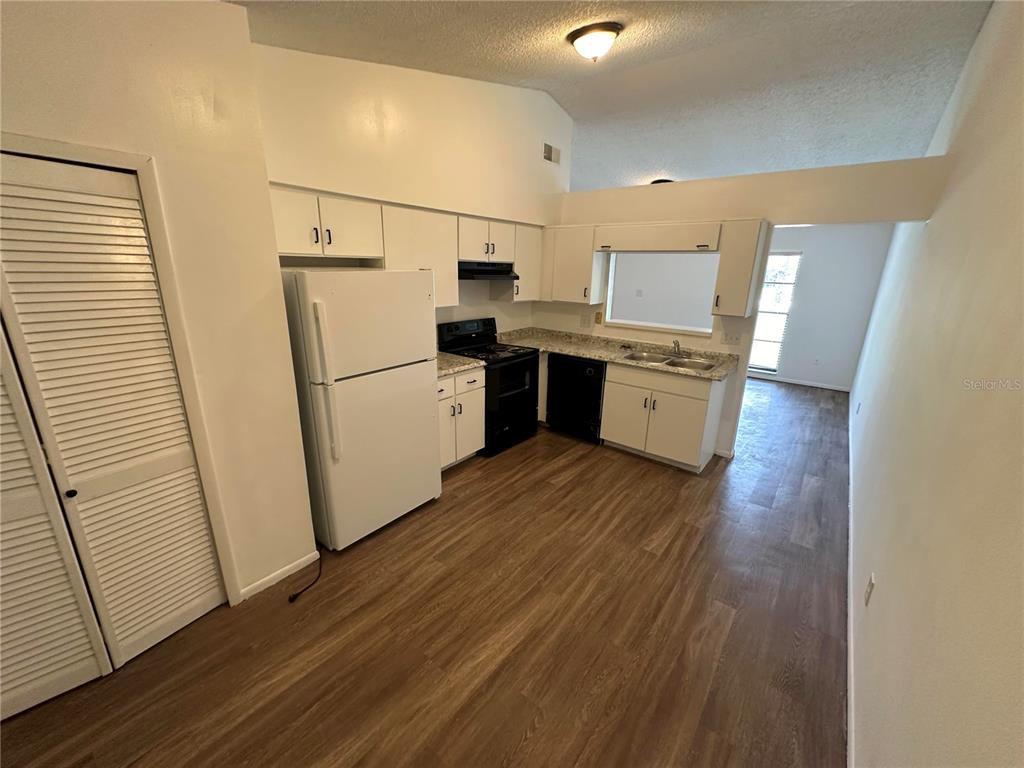 A kitchen with white cabinets, white appliances, a black stove, and wood-look flooring — 1928 BONNEVILLE DRIVE, ORLANDO, FL