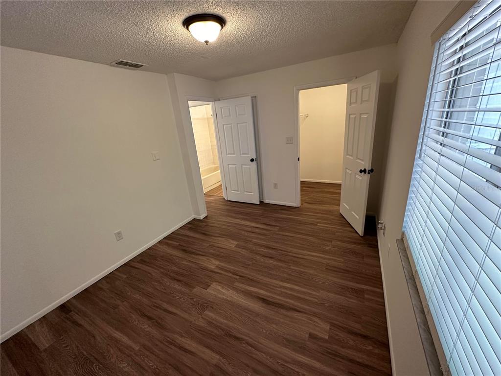 A bedroom with wood-look flooring, a ceiling light, a bathroom door, and a walk-in closet — 1928 BONNEVILLE DRIVE, ORLANDO, FL