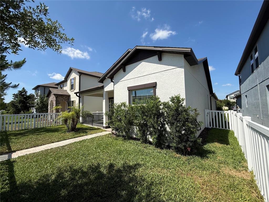 A white stucco house with a side porch and white vinyl fencing on a sunny day — 9601 FLOURISH DRIVE, LAND O LAKES, FL