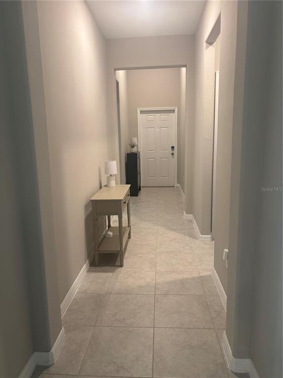 A hallway with light-colored tile flooring leads to a white front door — 9601 FLOURISH DRIVE, LAND O LAKES, FL