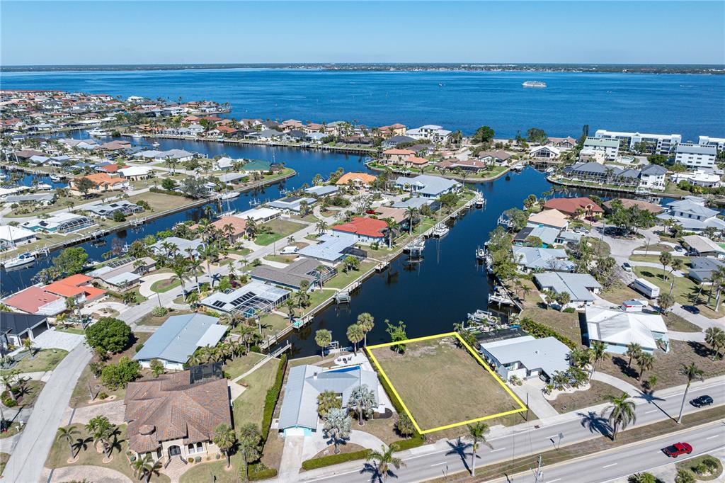 An aerial view shows a vacant waterfront lot outlined in yellow near a residential canal — 1940 W MARION AVENUE, PUNTA GORDA, FL
