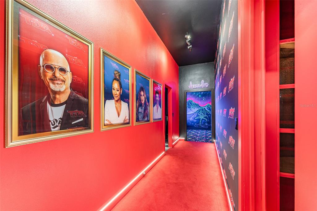 A red-carpeted hallway features framed celebrity portraits on one wall and a neon-lit arcade entrance — 1025 CASTLE PINES COURT, REUNION, FL