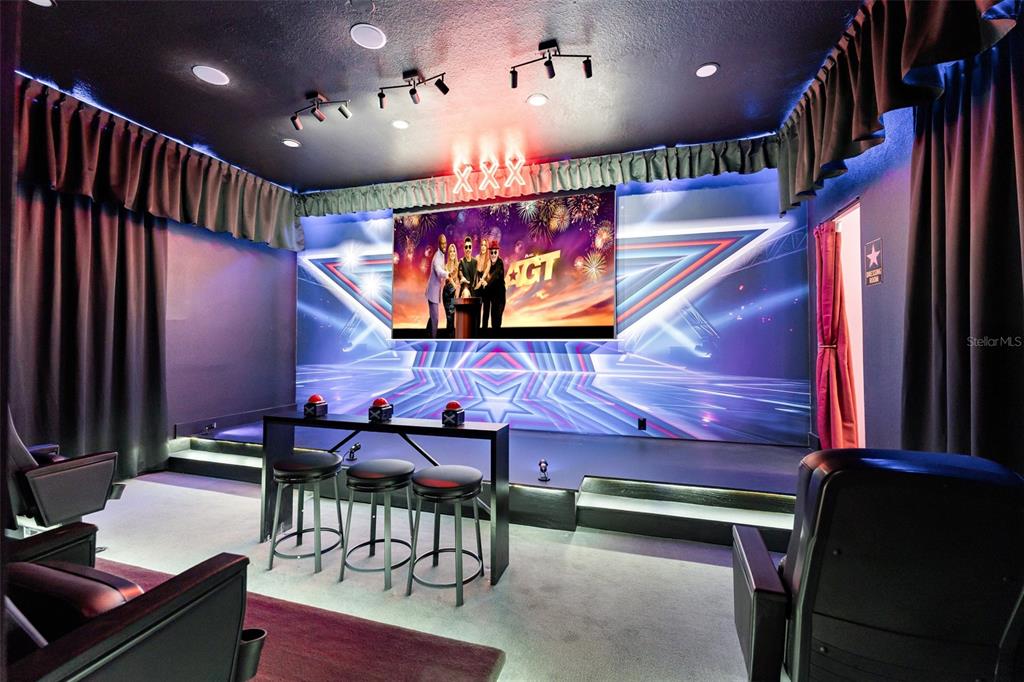 A home theater room features a stage, a large screen, and three red buzzers — 1025 CASTLE PINES COURT, REUNION, FL