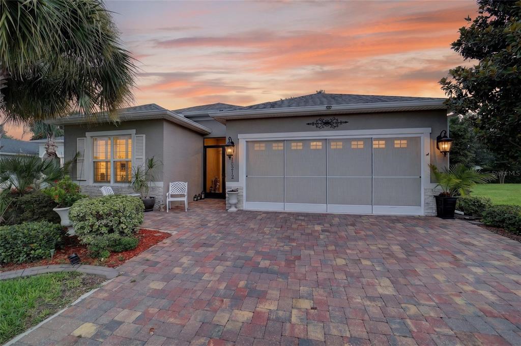A single-story house with a paved driveway, a garage screen, and a sunset sky — 10212 JULIA ISLES AVENUE, OXFORD, FL