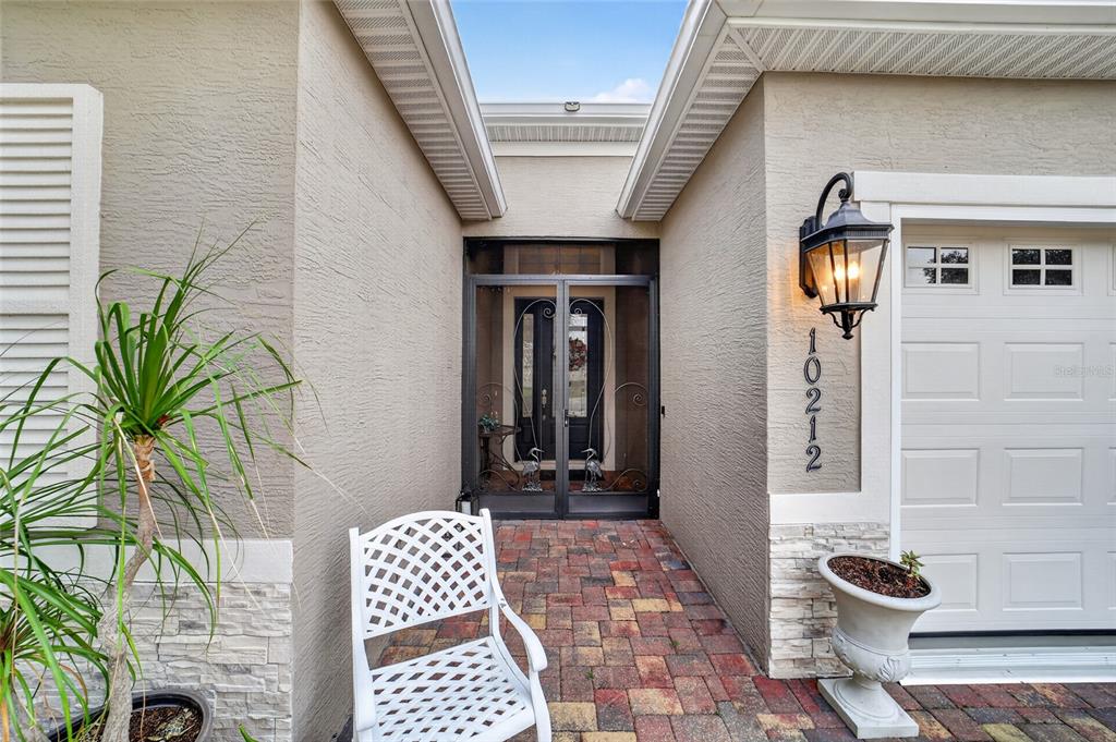 A front entryway features a paved walkway, a white chair, and a decorative screen door — 10212 JULIA ISLES AVENUE, OXFORD, FL