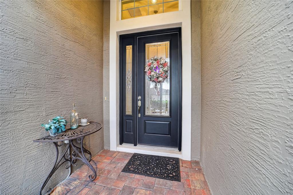 A black front door with a glass insert and wreath sits on a brick porch — 10212 JULIA ISLES AVENUE, OXFORD, FL