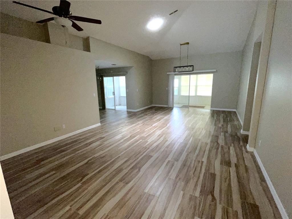 An open-concept living area features wood-look flooring, a vaulted ceiling, and sliding glass doors — 2222 MAYFIELD PALMS LANE UNIT 322, SUN CITY CENTER, FL