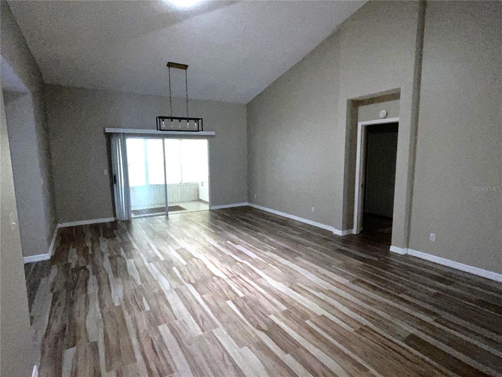 A living room with vaulted ceilings, wood-look flooring, a modern chandelier, and a sliding glass door — 2222 MAYFIELD PALMS LANE UNIT 322, SUN CITY CENTER, FL