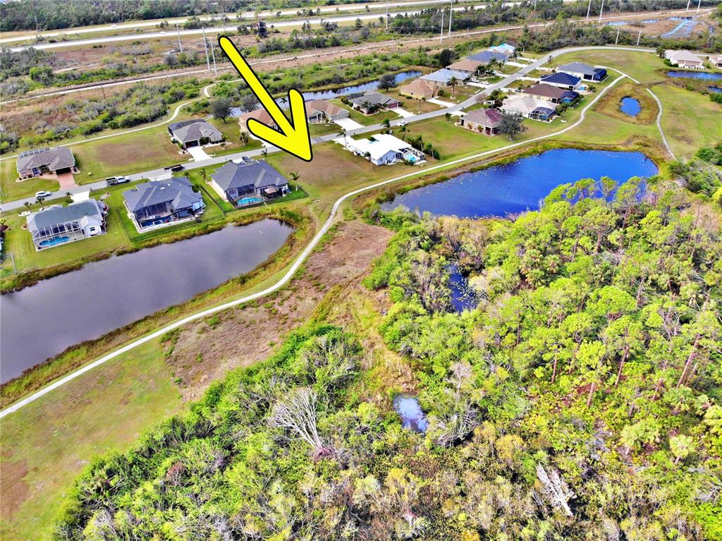 An aerial view shows a suburban neighborhood with houses, ponds, and surrounding wooded areas — 12932 SW PEMBROKE CIRCLE S, LAKE SUZY, FL