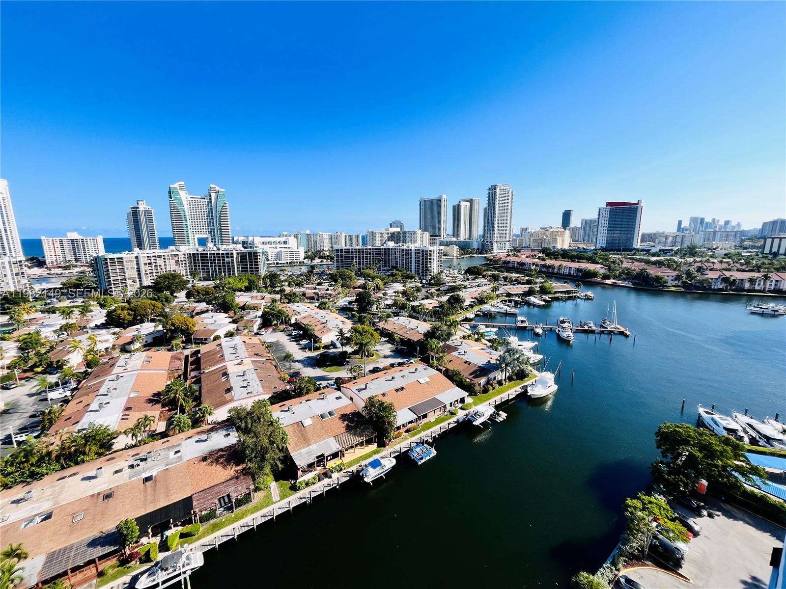 An aerial view shows a waterfront residential complex with docked boats and city skyscrapers — 2500 Parkview Dr # 1803, Hallandale Beach FL 33009, HALLANDALE BEACH, FL