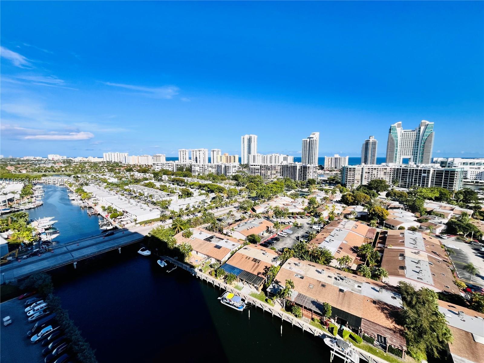 An aerial view shows a canal with boats, residential buildings, and a distant city skyline — 2500 Parkview Dr # 1803, Hallandale Beach FL 33009, HALLANDALE BEACH, FL