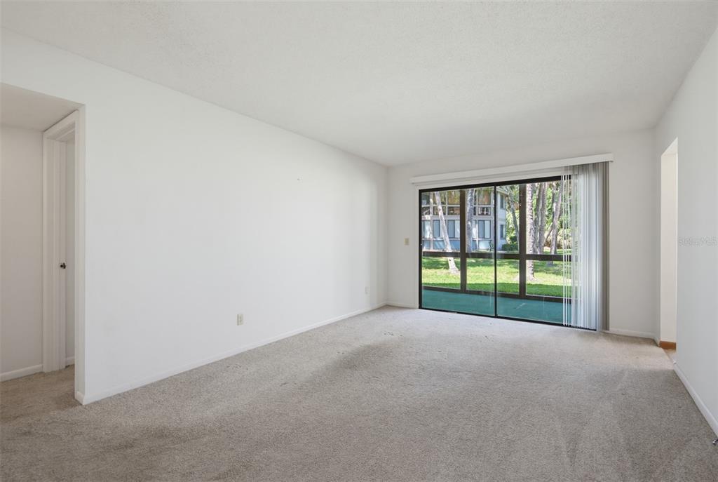 An empty living room with beige carpet, white walls, and a sliding glass door — 7 MID PINES CIRCLE, PALM COAST, FL