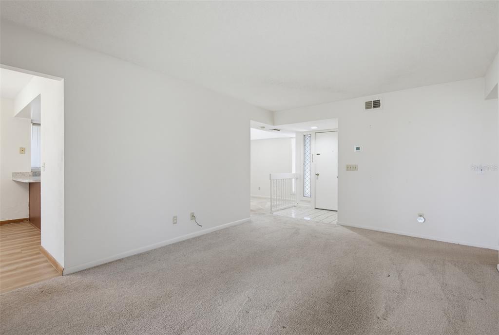 A carpeted living room with white walls leads to an entryway with a white door — 7 MID PINES CIRCLE, PALM COAST, FL