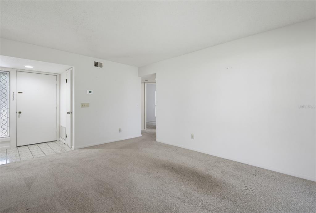 An interior view of a carpeted living area with a white front door and entryway — 7 MID PINES CIRCLE, PALM COAST, FL