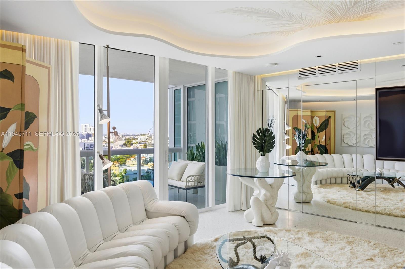 A modern living room features a white tufted sofa, glass-topped tables, and mirrored walls — 1000 S Pointe Dr # 1606, Miami Beach FL 33139, MIAMI BEACH, FL