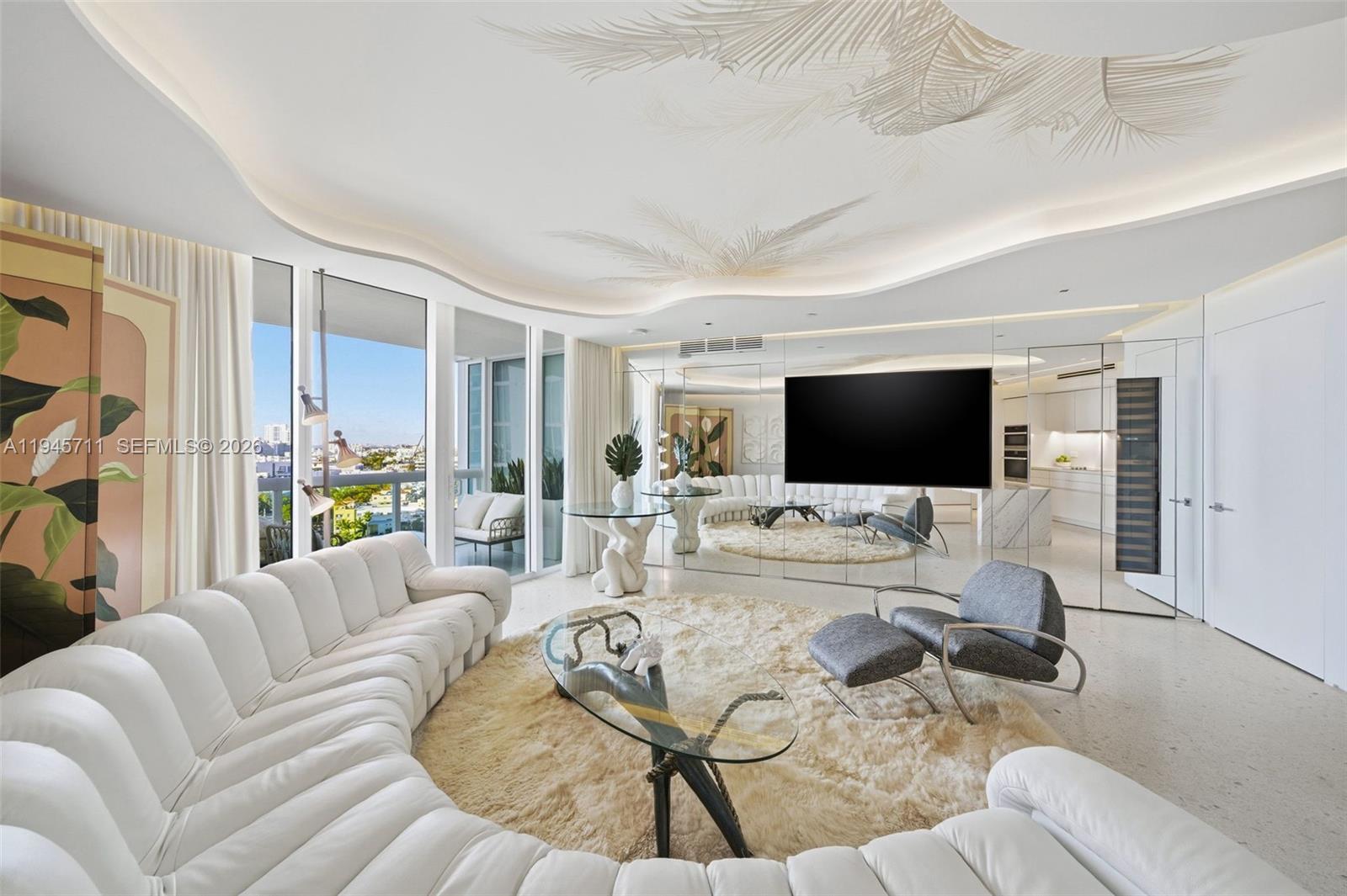 A modern living room features a curved white sofa, glass coffee table, and mirrored walls — 1000 S Pointe Dr # 1606, Miami Beach FL 33139, MIAMI BEACH, FL