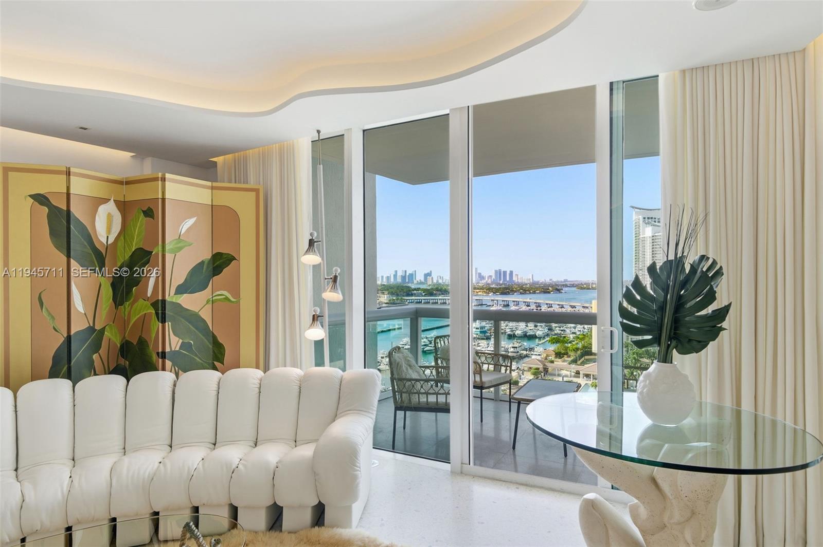 A living room features a white sofa, a folding screen, and a balcony overlooking water — 1000 S Pointe Dr # 1606, Miami Beach FL 33139, MIAMI BEACH, FL