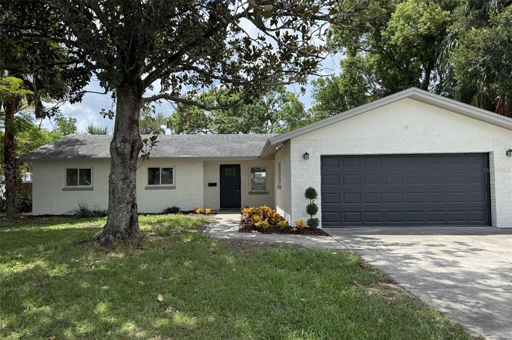 A single-story white brick house with a dark garage door and a large front tree — 779 PARK MANOR DRIVE, ORLANDO, FL