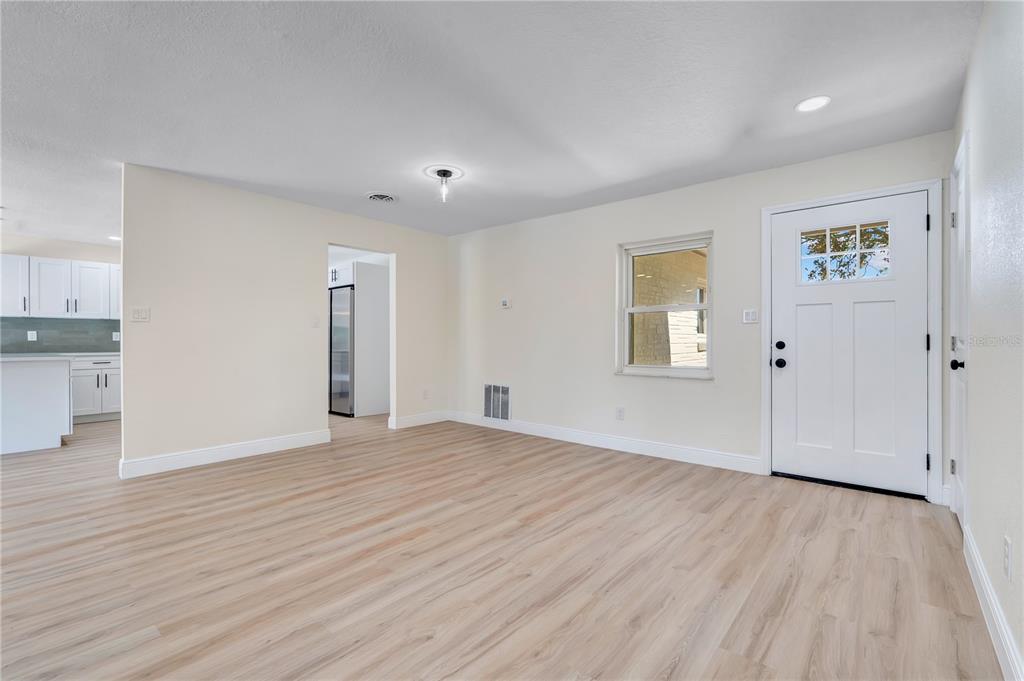 A bright living room features light wood-look flooring, white walls, and a white front door — 779 PARK MANOR DRIVE, ORLANDO, FL