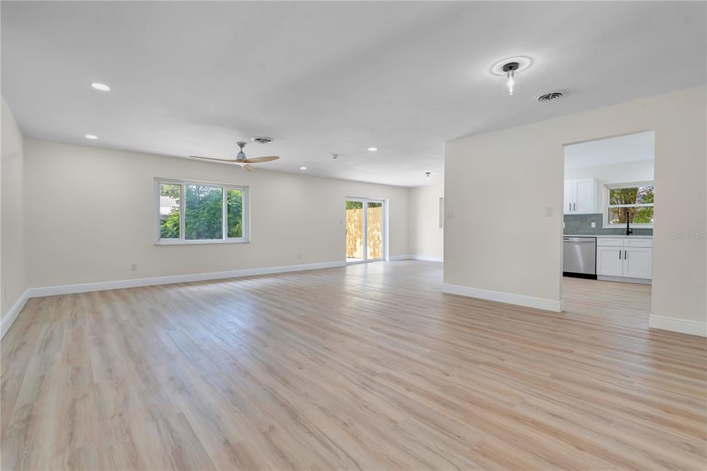 A spacious living room with light wood-look flooring leads into a kitchen with white cabinetry — 779 PARK MANOR DRIVE, ORLANDO, FL