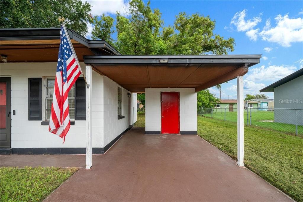 A white concrete block house features a covered carport with a bright red door — 1708 E OHIO STREET, PLANT CITY, FL