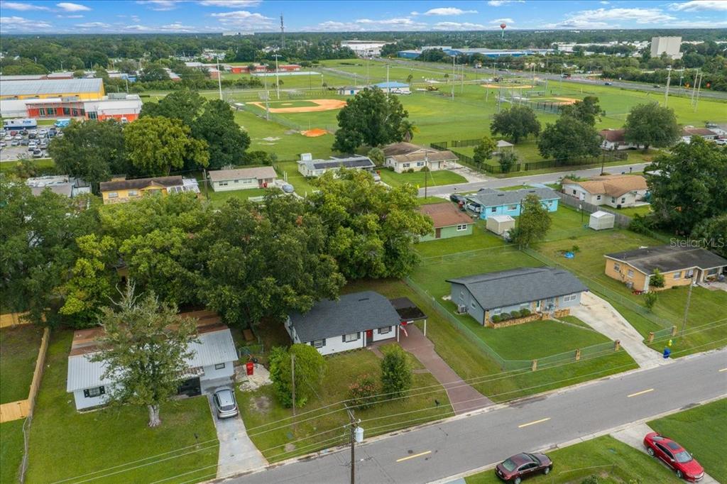 An aerial view shows several single-story houses with yards near a large grassy sports complex — 1708 E OHIO STREET, PLANT CITY, FL