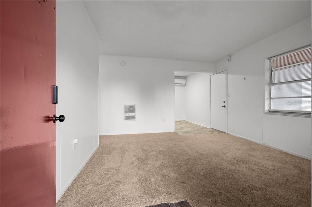 An empty room with beige carpet, white walls, a window with blinds, and a red door — 1708 E OHIO STREET, PLANT CITY, FL