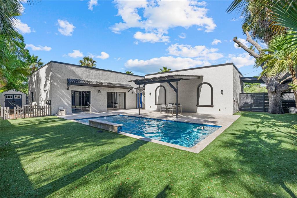 A backyard features a swimming pool, a covered patio, and a modern stucco house — 1185 S SHADE AVENUE, SARASOTA, FL