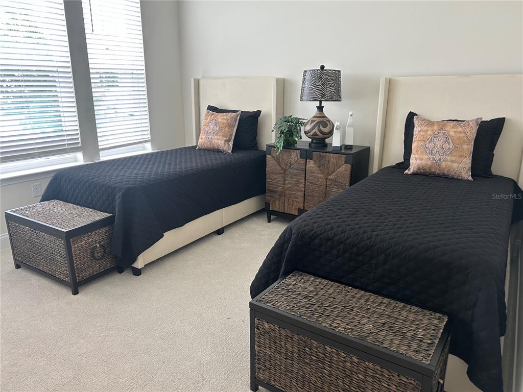 A bedroom features two twin beds with black quilts, matching storage trunks, and a nightstand — 3630 SW 118TH DRIVE, GAINESVILLE, FL