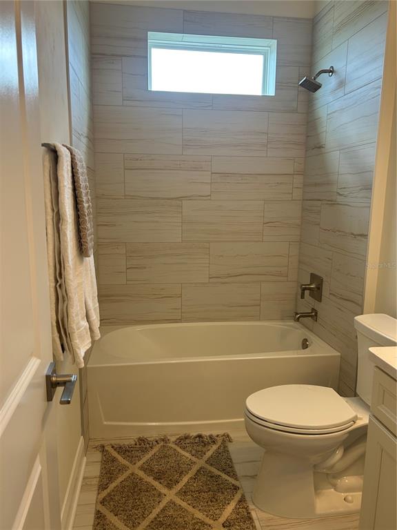 A bathroom features a white bathtub, a toilet, and walls tiled with light-colored horizontal planks — 3630 SW 118TH DRIVE, GAINESVILLE, FL