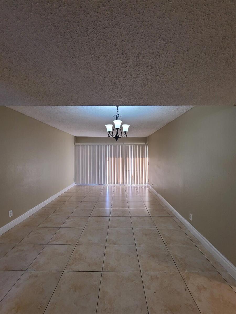 An empty dining room features beige walls, tile flooring, and a central chandelier — 1461 Windorah Way # G, West Palm Beach FL 33411, WEST PALM BEACH, FL