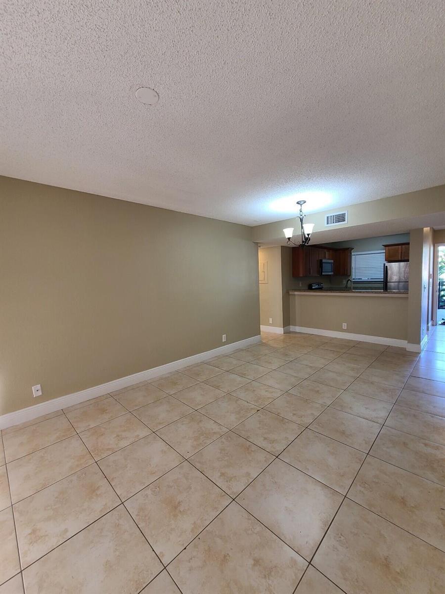 An open-concept living area with beige walls, tile flooring, and a view into the kitchen — 1461 Windorah Way # G, West Palm Beach FL 33411, WEST PALM BEACH, FL