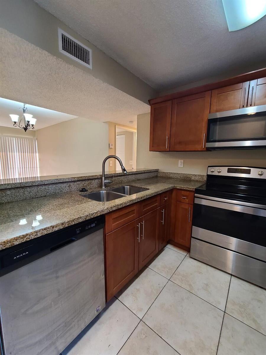 A kitchen features wood cabinets, granite countertops, stainless steel appliances, and tile flooring — 1461 Windorah Way # G, West Palm Beach FL 33411, WEST PALM BEACH, FL