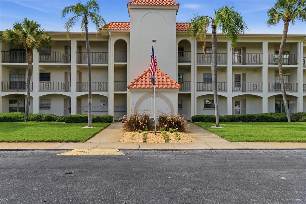 A three-story apartment building with a central entrance, a flagpole, and palm trees — 19029 US HIGHWAY 19 N UNIT 7-12, CLEARWATER, FL