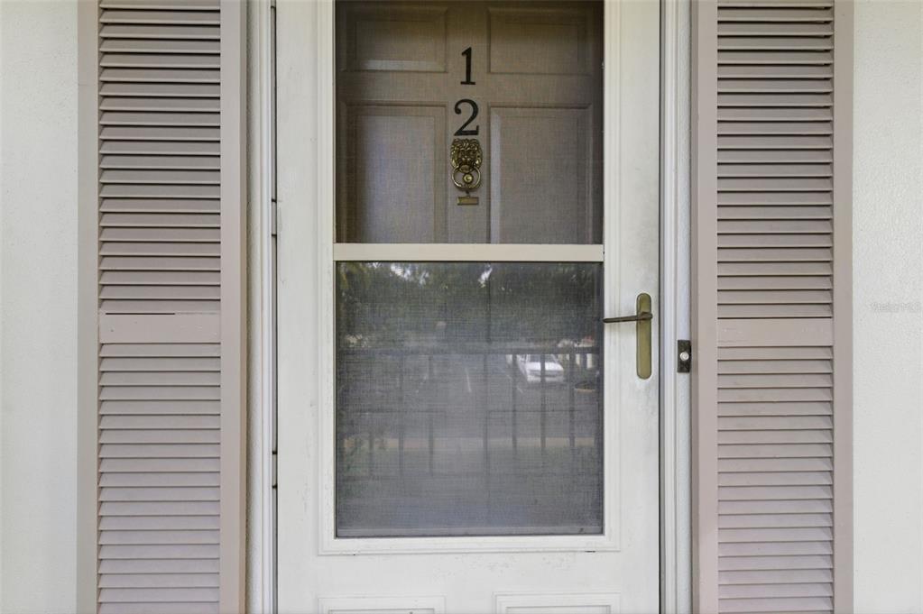A white storm door with a screen and house number sits between two louvered shutters — 19029 US HIGHWAY 19 N UNIT 7-12, CLEARWATER, FL