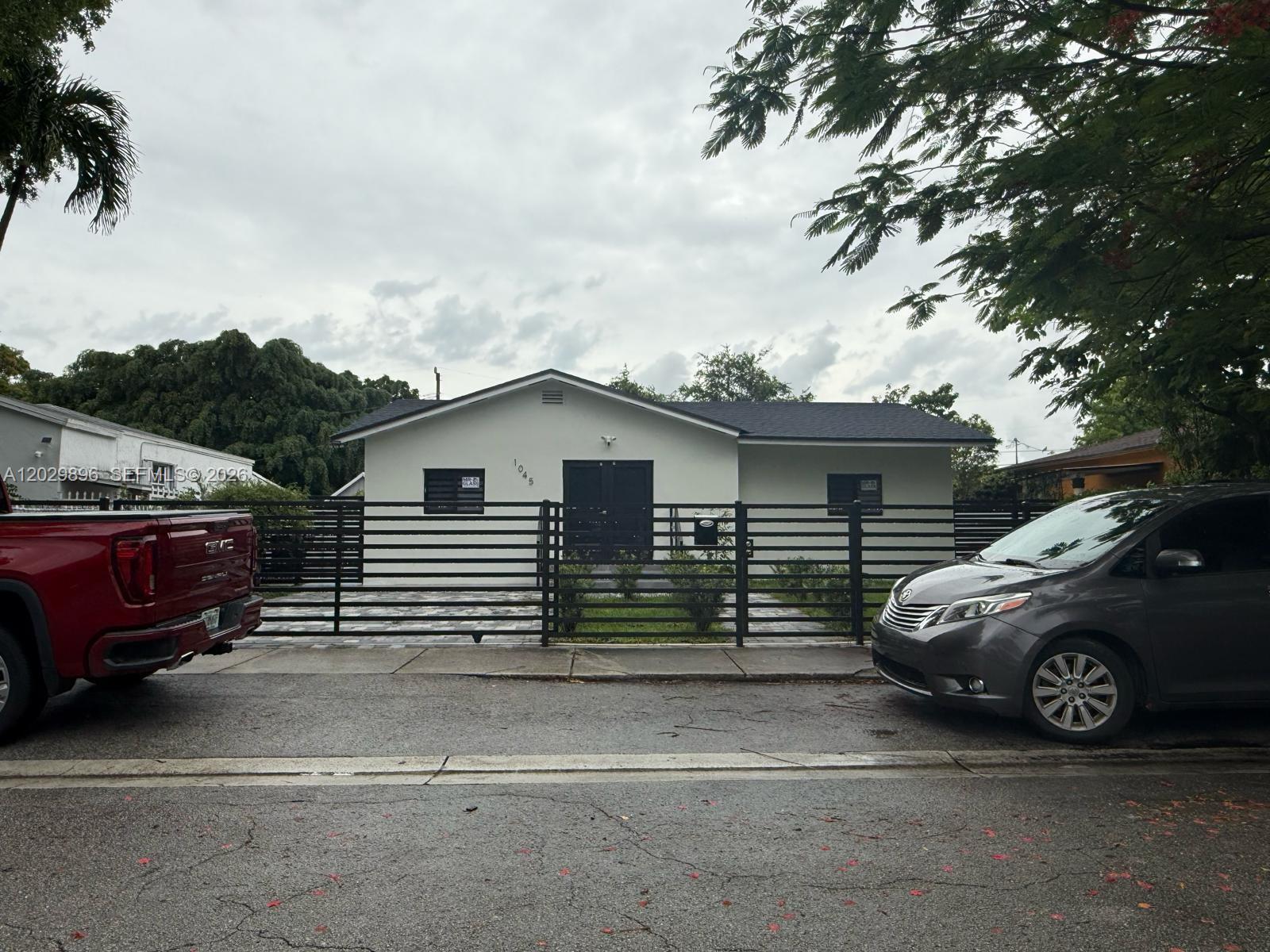 A single-story house with a black fence and a paved driveway sits behind a street — 1045 NW 58th Ter, Miami FL 33127, MIAMI, FL