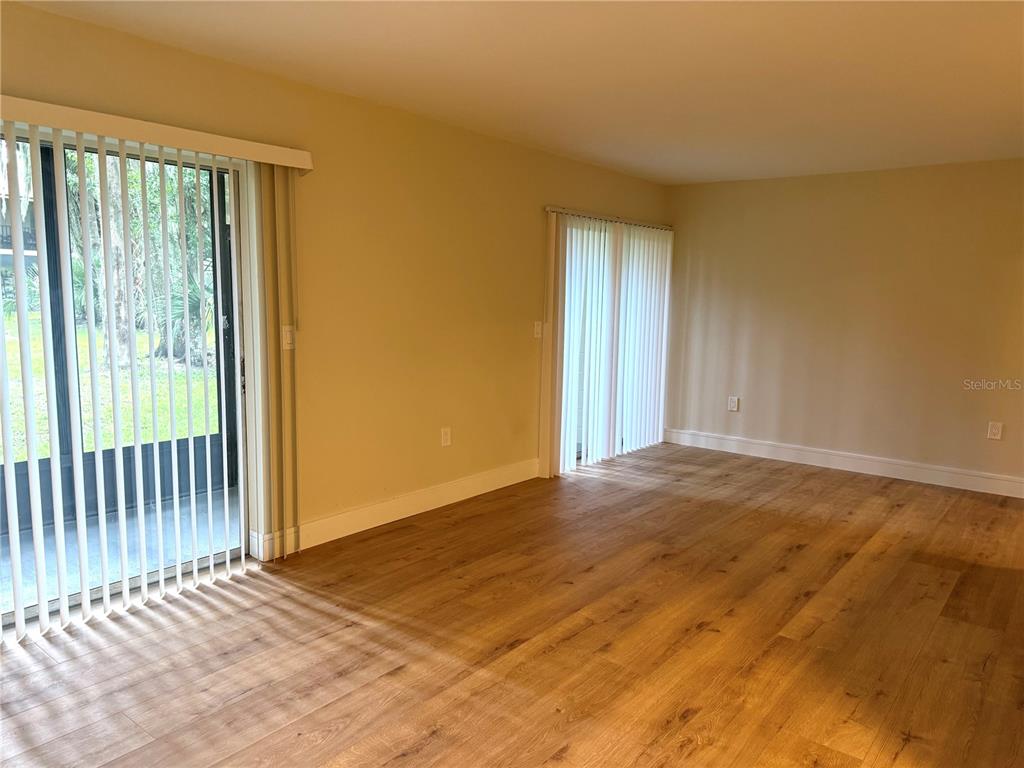 An empty room features light wood-look flooring, beige walls, and two sets of vertical blinds — 120 HIBISCUS WOODS COURT UNIT 9C, DELTONA, FL