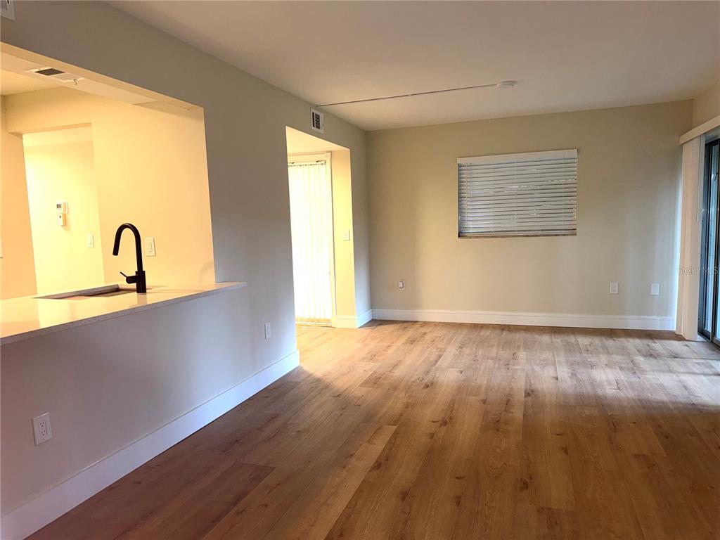 An interior view of a living area with wood-look flooring and a kitchen pass-through window — 120 HIBISCUS WOODS COURT UNIT 9C, DELTONA, FL