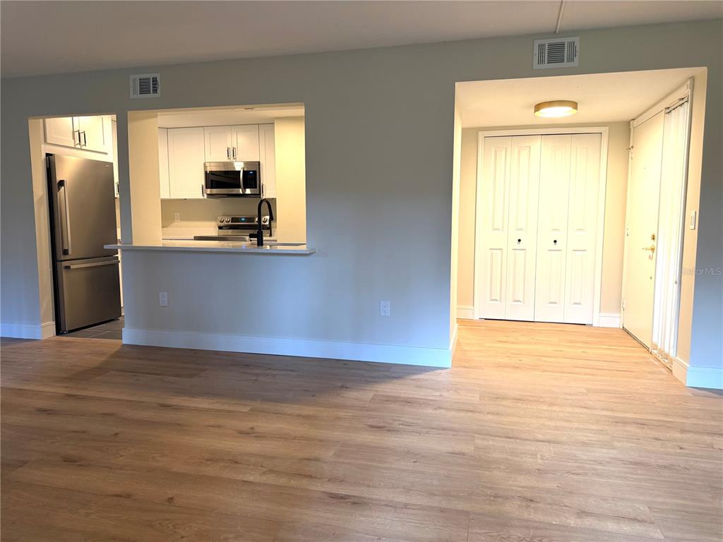 A view of a kitchen with white cabinets and stainless appliances opening to a living area — 120 HIBISCUS WOODS COURT UNIT 9C, DELTONA, FL