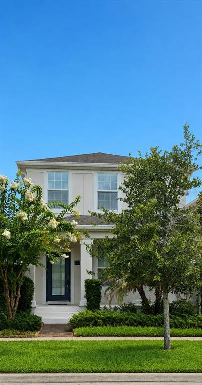 A two-story house with a front porch, dark blue door, and surrounding trees under blue sky — 12156 PHILOSOPHY WAY, ORLANDO, FL