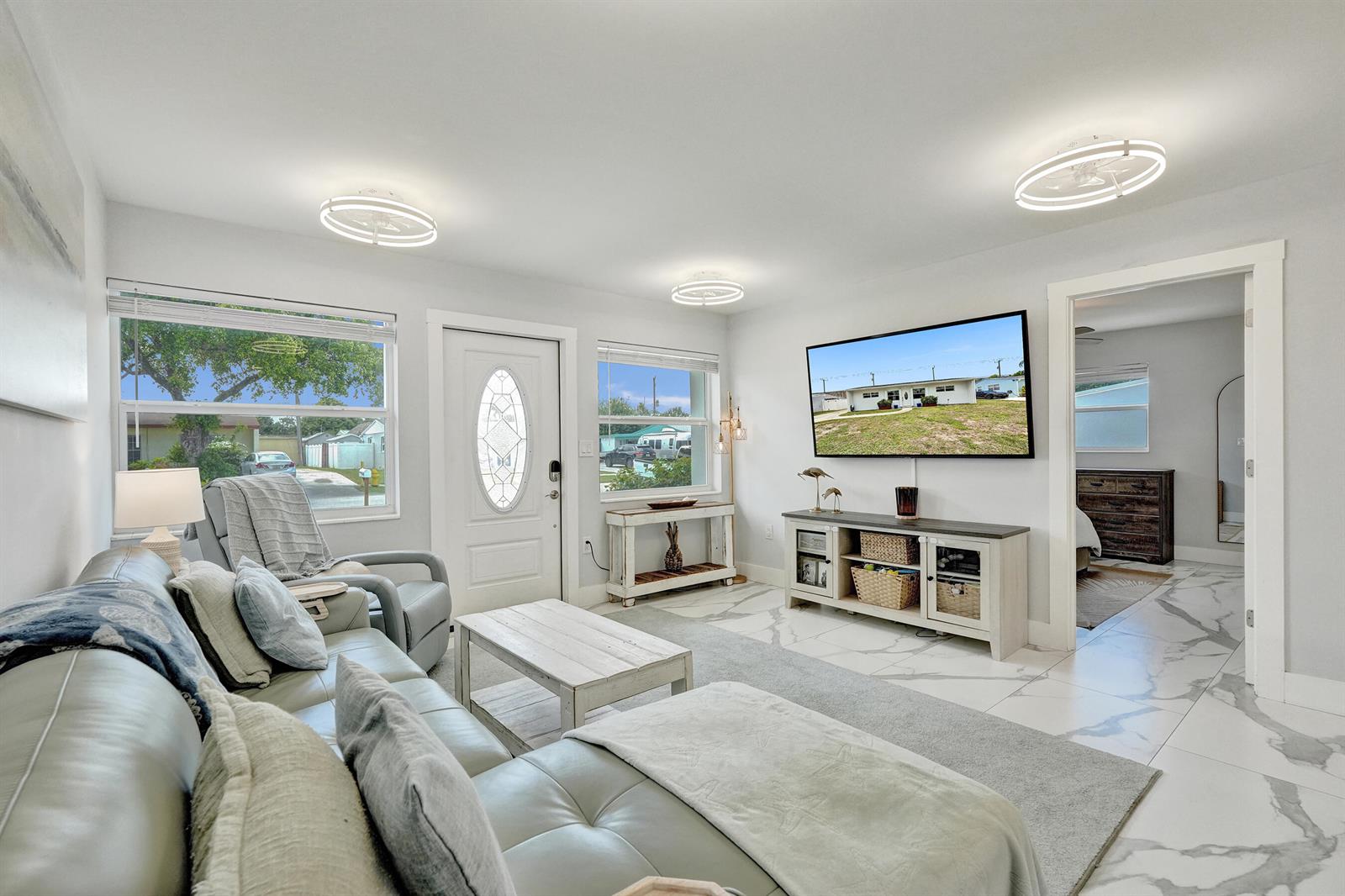 A living room features light gray leather furniture, a wall-mounted television, and white marble flooring — 9446 Birmingham Drive, Palm Beach Gardens FL 33410, PALM BEACH GARDENS, FL