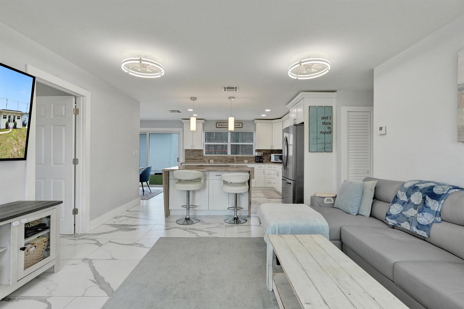 An open-concept living room and kitchen featuring white cabinetry, marble-look tile flooring, and a sectional — 9446 Birmingham Drive, Palm Beach Gardens FL 33410, PALM BEACH GARDENS, FL