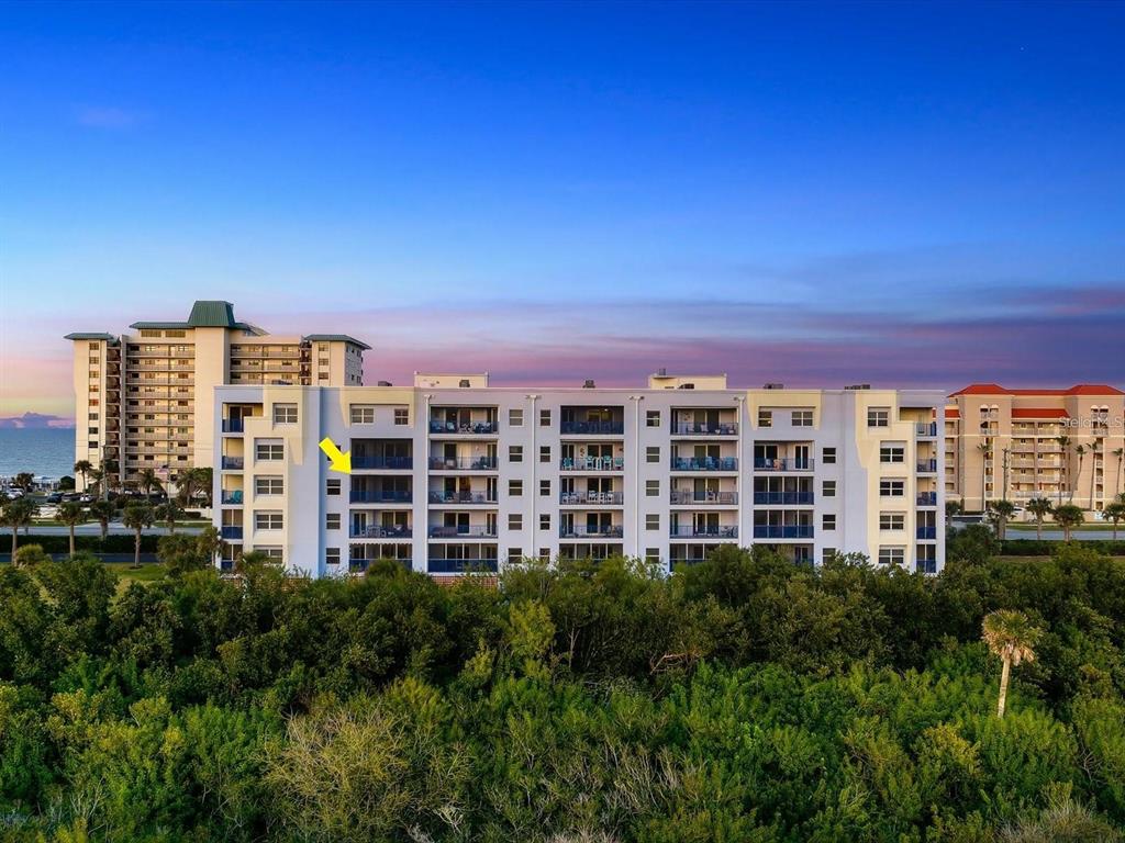 An exterior view of a multi-story beachfront condominium building surrounded by dense green trees — 5300 SOUTH ATLANTIC AVENUE UNIT 19406, NEW SMYRNA BEACH, FL