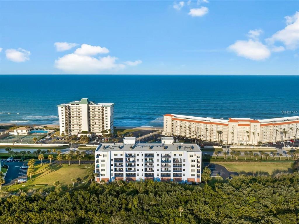 An aerial view shows three multi-story apartment buildings situated along a sandy beach and ocean — 5300 SOUTH ATLANTIC AVENUE UNIT 19406, NEW SMYRNA BEACH, FL